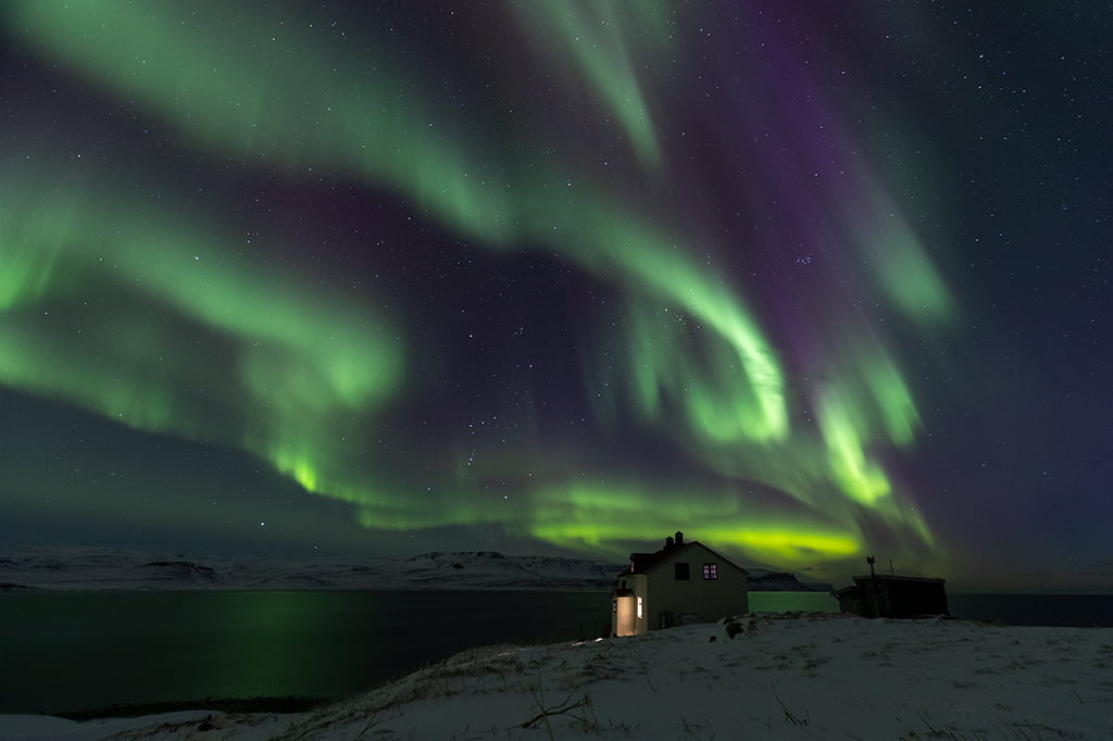 Northern lights dancing in the night sky over a cabin in west Iceland